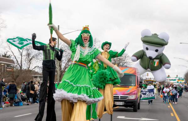 A group of stilt walkers dressed in green performing down the street in the St. Patrick's Day Parade.