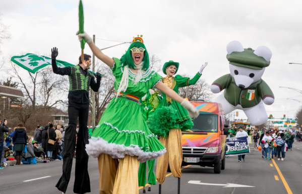 A group of stilt walkers dressed in green performing down the street in the St. Patrick's Day Parade.
