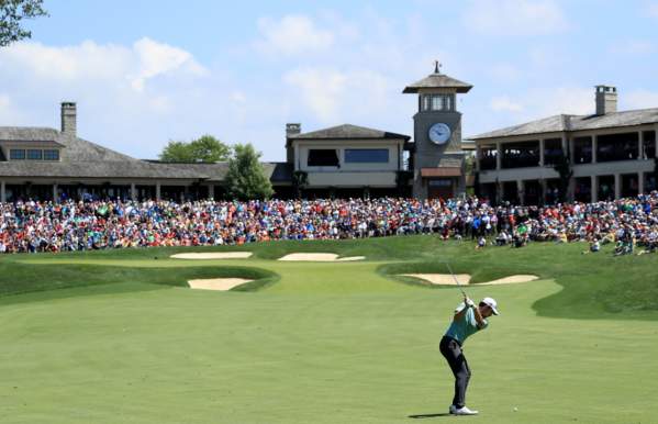 Golfer swining club at golf ball towards the 18th green that is surrounded by a crowd at the Memorial Touranemnt.