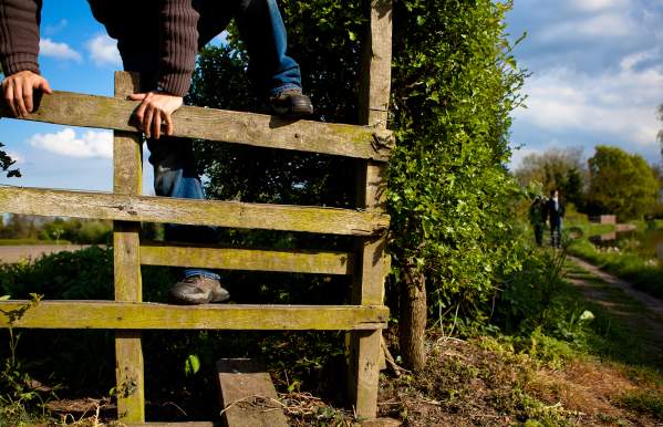 Person climbing over wooden stile beside canal footpath