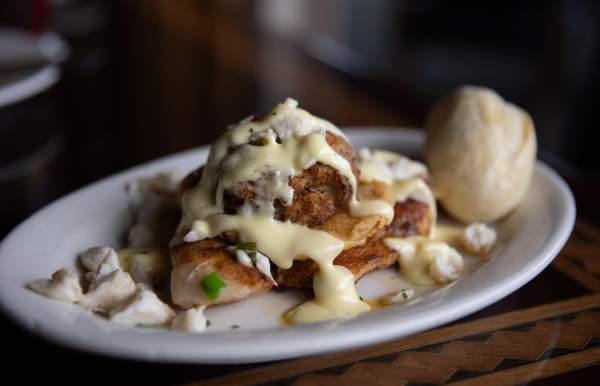 Blackened fish with cream sauce and lump crab meat and a roll on a white oval plate