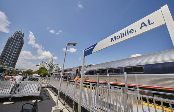 Amtrak train at the Mobile, Alabama station with passengers boarding, set against the downtown skyline including the RSA Tower and Arthur R. Outlaw Convention Center.