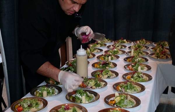 plates of food lined up on a table with chef adding sauces