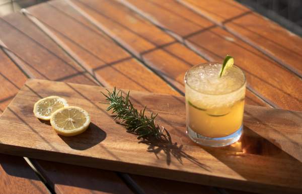 cocktail sitting on a wooden paddle with rosemary and lemon slices