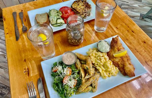 two plates of food on a table - fish, mac and cheese, fries, greens