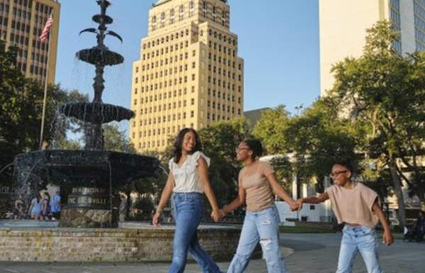 A mother and two girls walking near a fountain in front of skyscrapers