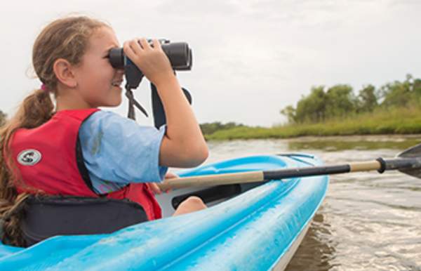 young girl in a kayak looking through binoculars