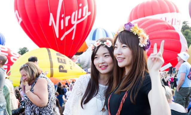 Two women wearing flower crowns standing in front of ascending balloons at Bristol International Balloon Fiesta - credit Paul Box