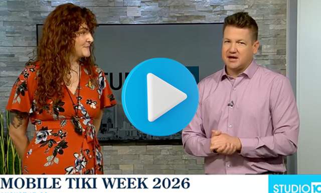 A woman with long hair wearing a red flowered dress and a man with a red button down shirt on a TV studio set that says Mobile Tiki Week 2026 August 17 - 22