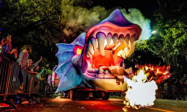 A purple and blue Mardi Gras dragon float breathes fire while on a parade route
