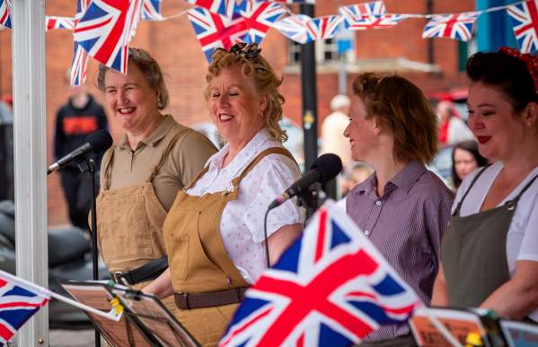 Group of women in vintage costumes surrounded by Union Jack flag bunting