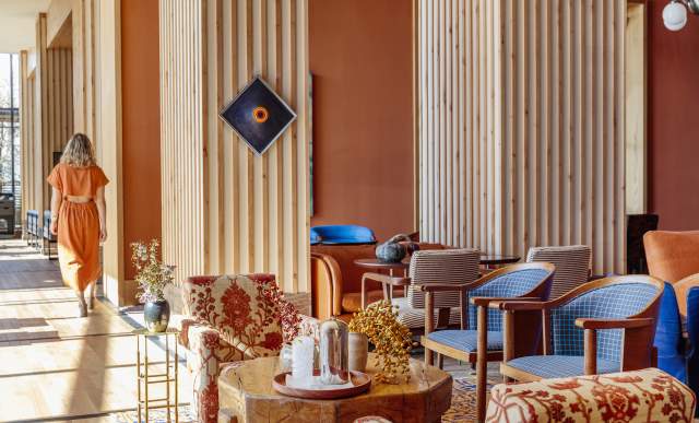 Woman in an orange dress walking past a curated collection of vintage furniture in the Austin Proper hotel lobby.