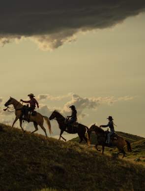 Three people riding horse up a hill.