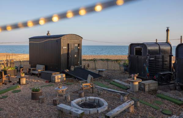 Two sauna sheds on the shingle beach, surrounding a campfire in Brighton