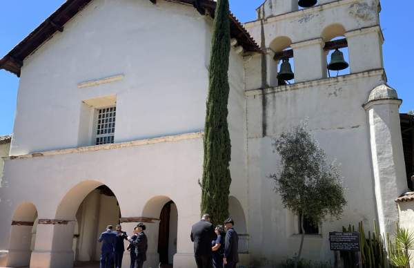 San Juan Bautista Mission. People stand in front of the Mission entryway and Bell Tower.