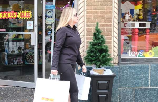 A woman holding a shopping bag and walking along a sidewalk in front of a store. Some holiday decorations are in front of the shop.