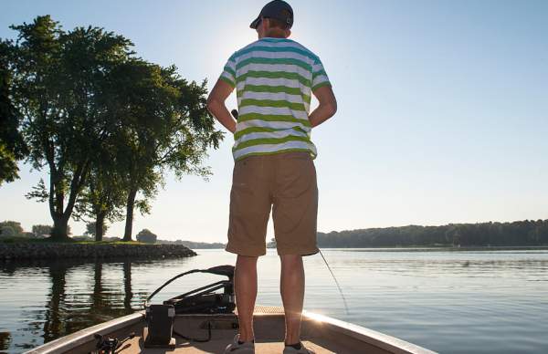 man standing on boat with tan shorts and green/white striped shirt fishing