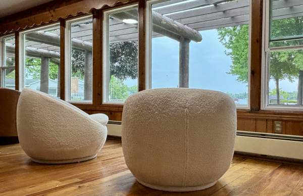 Two cream retro themed chairs in front of a floor to ceiling windows over looking a lake.