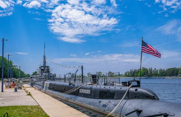 world war II submarine docked in channel. blue skies with white clouds, american flag flying