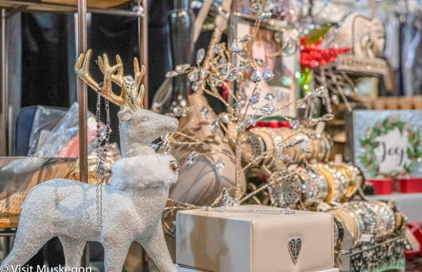 store holiday display of of white and sparkly deer with fur collar and gold antlers stands before display of shiny bracelets and leather purse and box