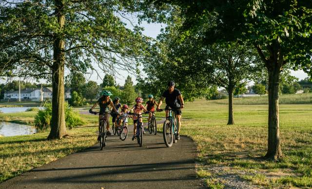 A group of people, including children, riding bicycles together on a paved path in a scenic park during a sunny day.