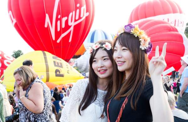 Two women wearing flower crowns standing in front of ascending balloons at Bristol International Balloon Fiesta - credit Paul Box
