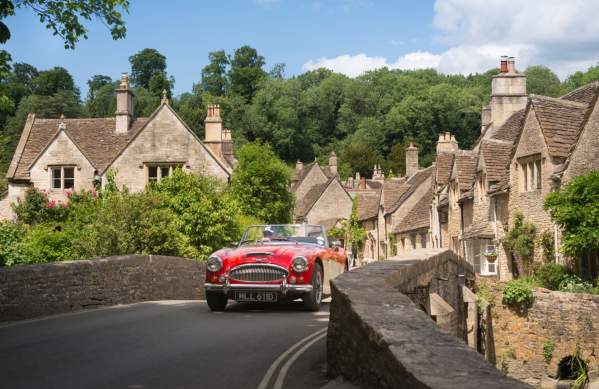 A red vintage sports car driving over the bridge in the village of Castle Combe, near Bristol - credit Great West Way