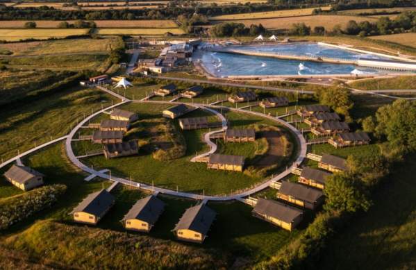 An aerial drone shot of The Wave and Camp at The Wave showing lodges and the Wave surfing lake in the background
