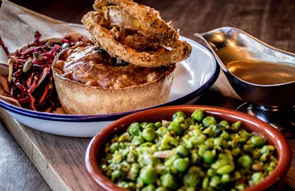A pie and salad on a plate with a gravy boat and separate bowl of peas at Pieminister Bristol - credit Pieminister