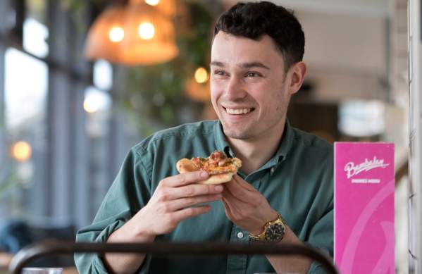 A male university student eating a pizza at Bambalan - credit Bambalan