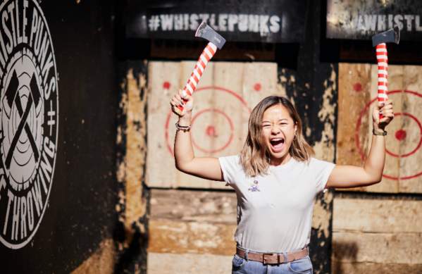 A woman cheering while holding two axes at the Whistle Punks Bristol Axe Throwing experience - credit Whistle Punks