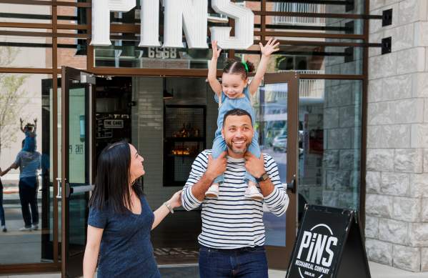 A family walking out of PINS Mehanical with the little girl cheering while riding on her dad's shoulders.