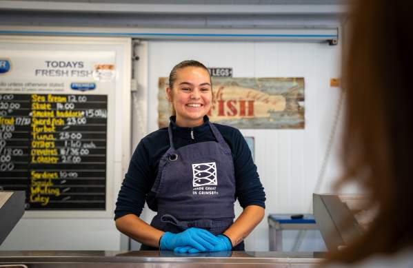 A smiling woman selling fish behind a counter.