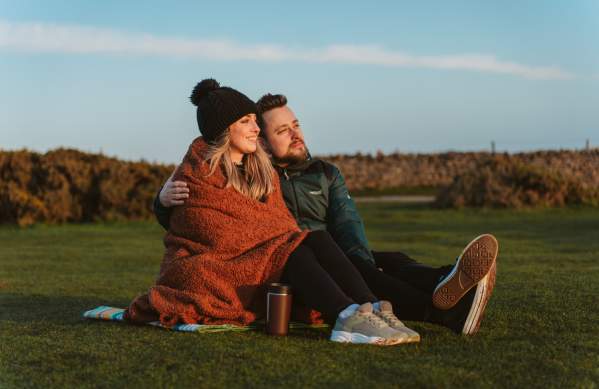 Young couple under a blanket with a coffee watching a sunset at rhossili bay in the winter