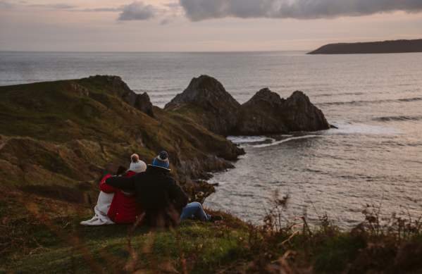 family keeping warm under a blanket with coffee looking out over three cliffs bay