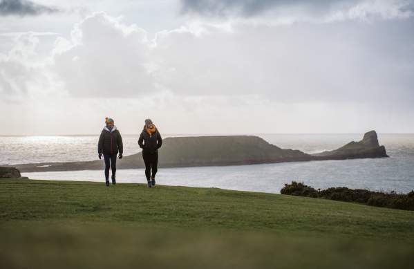 two young women walking along the coast with worms head in the background
