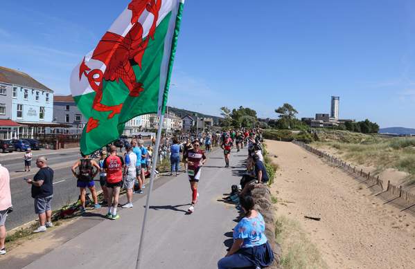 crowd cheering on competitors running along the swansea beach front during the Ironman Swansea event