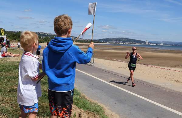 Two young boys cheering on their mum running along the race course waving welsh flags