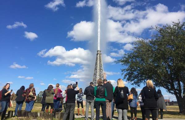 Visitors watch the gusher blow against a blue sky