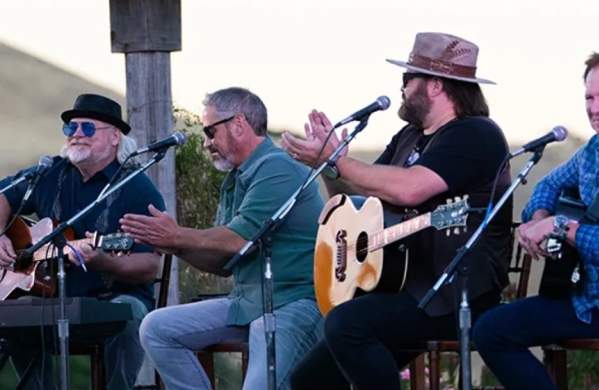 Four Musicians actively performing by singing, playing guitars, and clapping their hands.