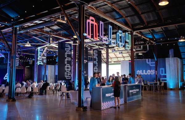 Interior of Fair Market venue with people standing at a registration desk in the foreground and attendees seated in auditorium-seating in the background