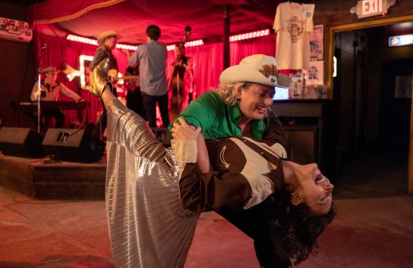 Two women in Western attire country dancing in a dance hall.