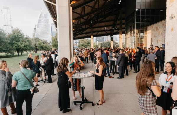 People with event badges on standing under the pavilion at Palmer Events Center during golden hour.