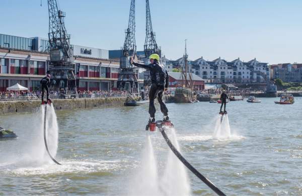 A man wearing a water-powered jetpack performing stunts on Bristol's Harbourside during the Bristol Harbour Festival with the M Shed local history museum in the background - credit Jim Cossey