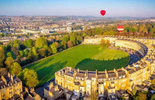 An aerial view of the Royal Crescent in Bath near Bristol, with hot air balloons launching from the green