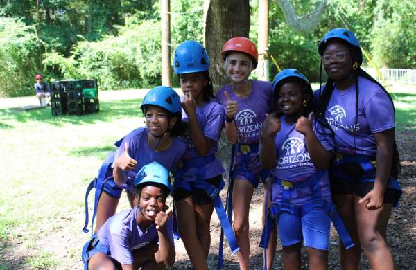 A group of girls pose for a photo while wearing helmets at the Challenge Course.