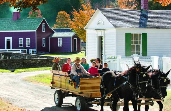 an image of a horse drawn carriage carrying people in front of historic houses with fall leaves behind it