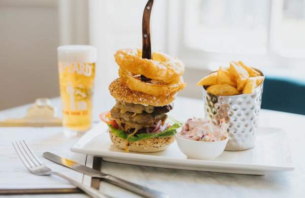 a plate with a burger and fries with a pint of beer in the background on a table in a white-lit restaurant