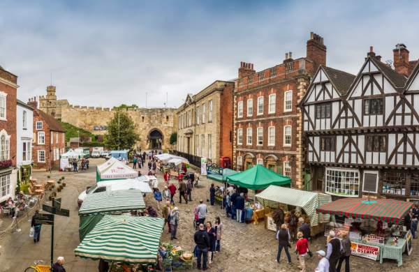 A farmers market outside of Lincoln Castle busy with stalls and people.