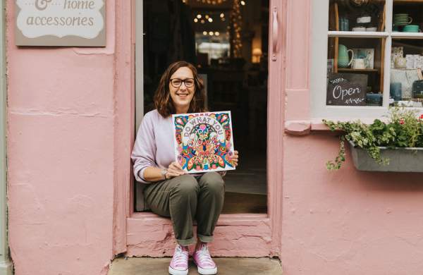Woman sat outside her gift shop holding a shop local sign